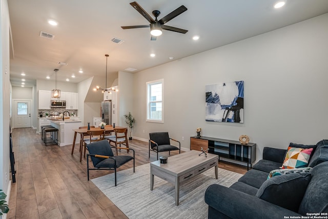 living room featuring sink, light hardwood / wood-style floors, and ceiling fan with notable chandelier