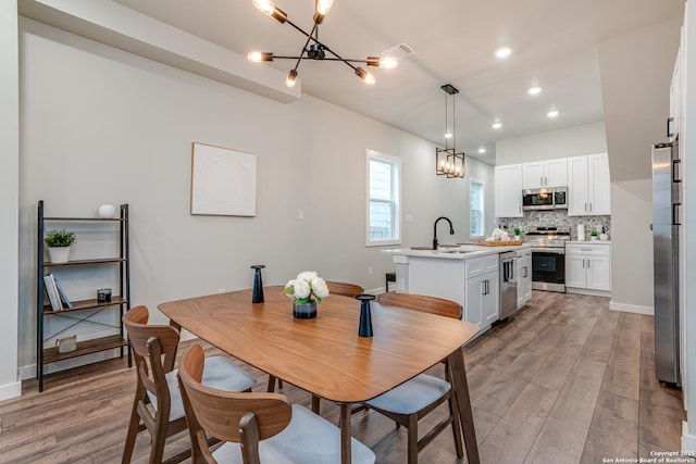 dining room featuring sink, a chandelier, and light hardwood / wood-style floors