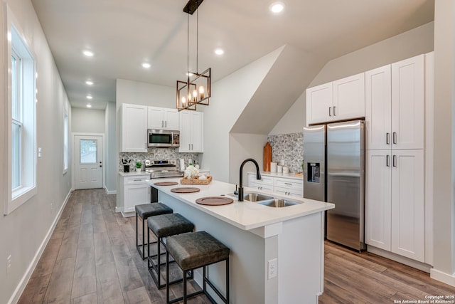 kitchen featuring appliances with stainless steel finishes, backsplash, sink, a center island with sink, and white cabinetry