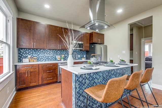 kitchen with a center island, a breakfast bar area, light hardwood / wood-style floors, island range hood, and stainless steel appliances