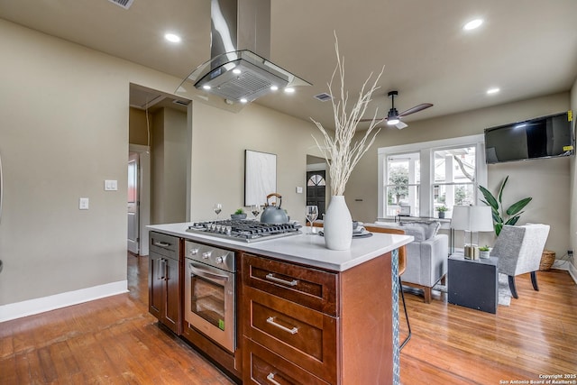 kitchen featuring island exhaust hood, light wood-type flooring, stainless steel appliances, ceiling fan, and a center island