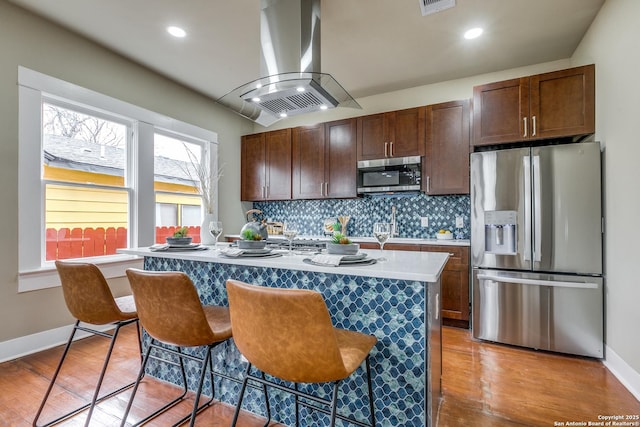 kitchen featuring appliances with stainless steel finishes, a wealth of natural light, island range hood, a center island with sink, and a breakfast bar area