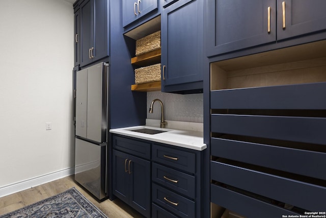 kitchen with blue cabinetry, stainless steel refrigerator, sink, and light hardwood / wood-style flooring