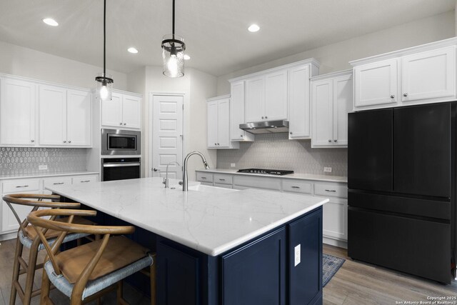 kitchen featuring white cabinets, a center island with sink, sink, decorative light fixtures, and stainless steel appliances