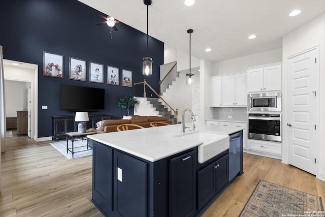 kitchen with white cabinets, sink, light wood-type flooring, an island with sink, and appliances with stainless steel finishes