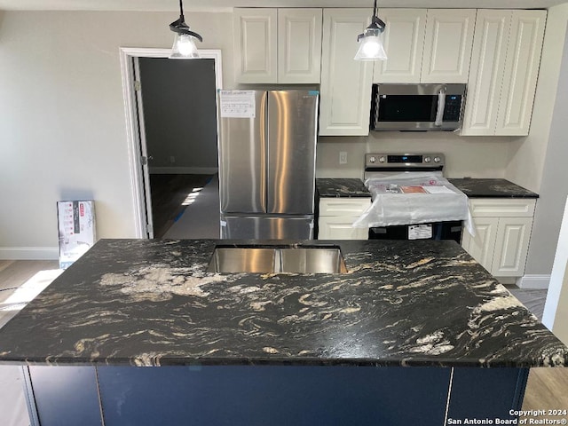 kitchen featuring dark stone counters, white cabinets, hanging light fixtures, appliances with stainless steel finishes, and light hardwood / wood-style floors