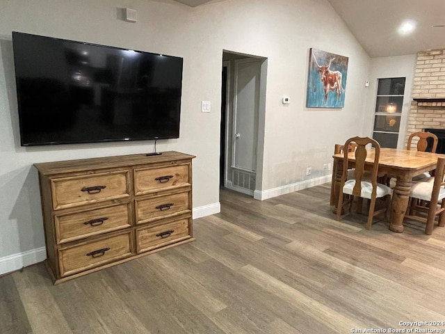 dining room featuring hardwood / wood-style flooring, lofted ceiling, and a brick fireplace