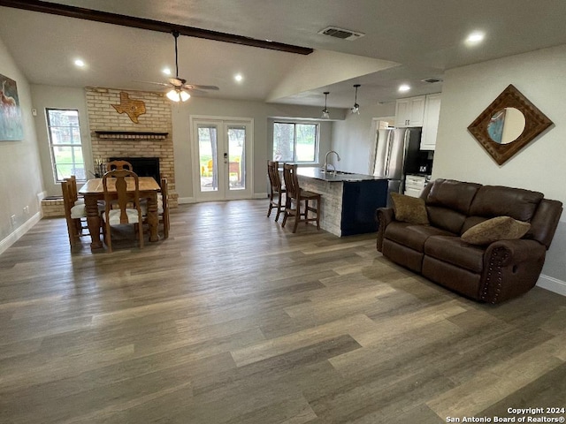 living room featuring ceiling fan, sink, dark hardwood / wood-style flooring, lofted ceiling with beams, and a fireplace