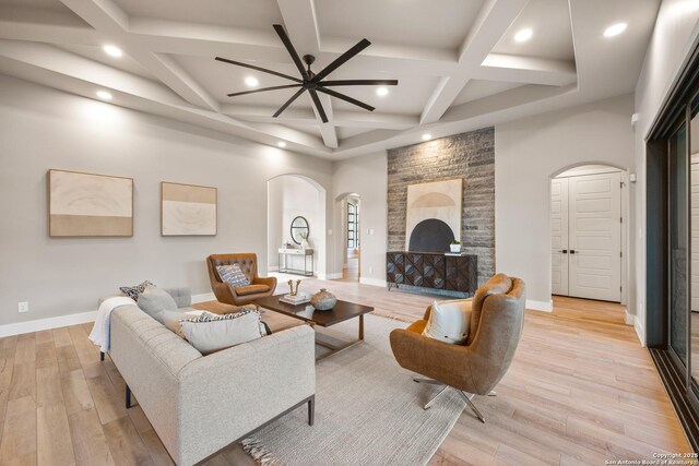 living room featuring ceiling fan, coffered ceiling, a brick fireplace, beamed ceiling, and light wood-type flooring