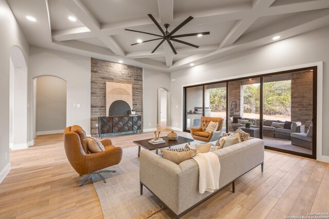 living room featuring a high ceiling, light hardwood / wood-style floors, a stone fireplace, and ceiling fan