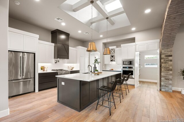 kitchen featuring white cabinetry, sink, light hardwood / wood-style floors, a center island with sink, and appliances with stainless steel finishes