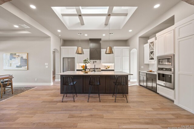 kitchen featuring decorative light fixtures, an island with sink, appliances with stainless steel finishes, and a skylight