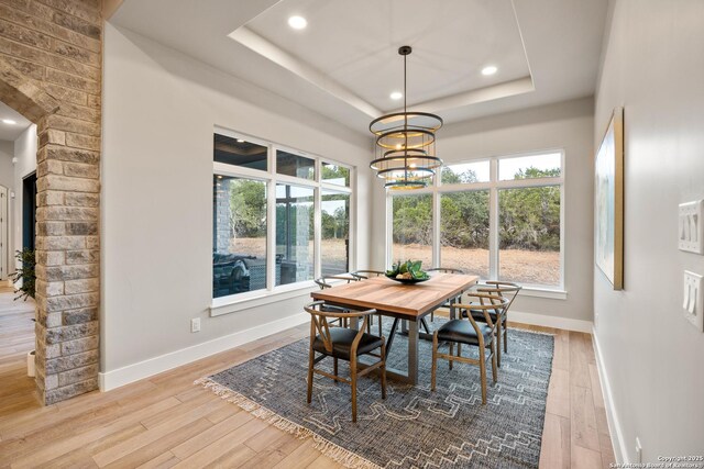 dining area featuring light wood-type flooring, a raised ceiling, and a healthy amount of sunlight