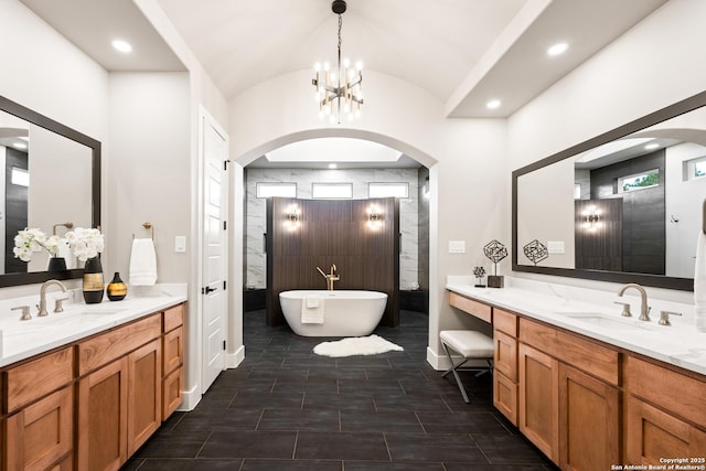 bathroom with a bathing tub, lofted ceiling, vanity, and a notable chandelier