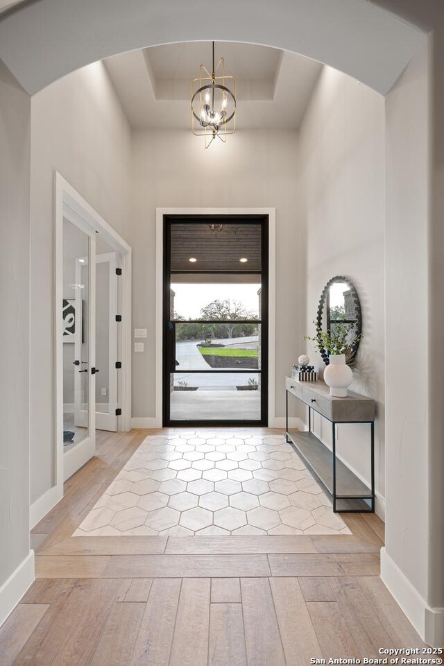 entryway featuring light hardwood / wood-style floors, a tray ceiling, and a notable chandelier