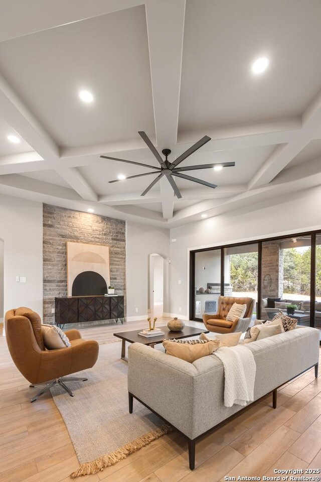 living room featuring coffered ceiling, ceiling fan, a stone fireplace, and light hardwood / wood-style flooring