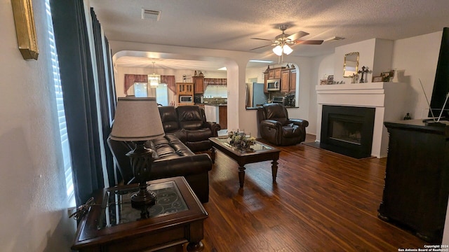 living room featuring a textured ceiling, ceiling fan, and dark wood-type flooring