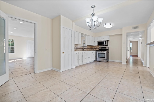 kitchen with appliances with stainless steel finishes, tasteful backsplash, an inviting chandelier, white cabinetry, and light tile patterned flooring