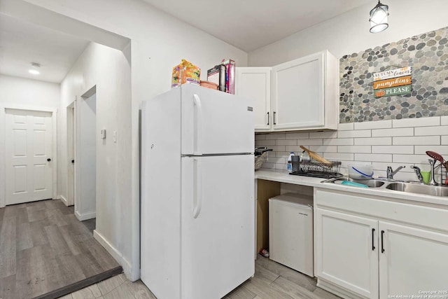 kitchen with white refrigerator, sink, light wood-type flooring, tasteful backsplash, and white cabinetry