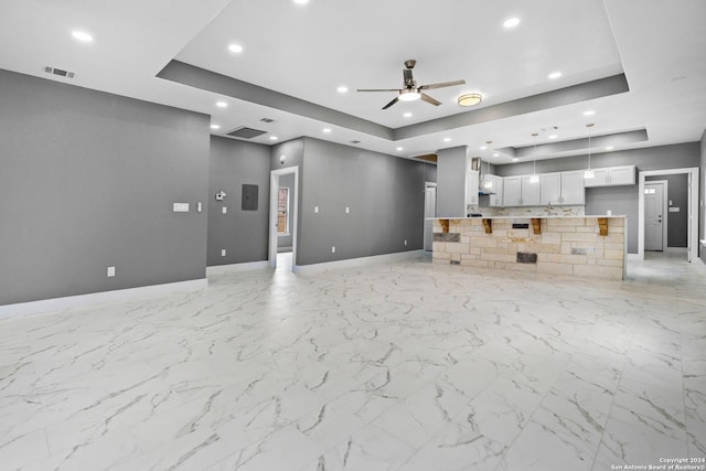 unfurnished living room with ceiling fan and a tray ceiling