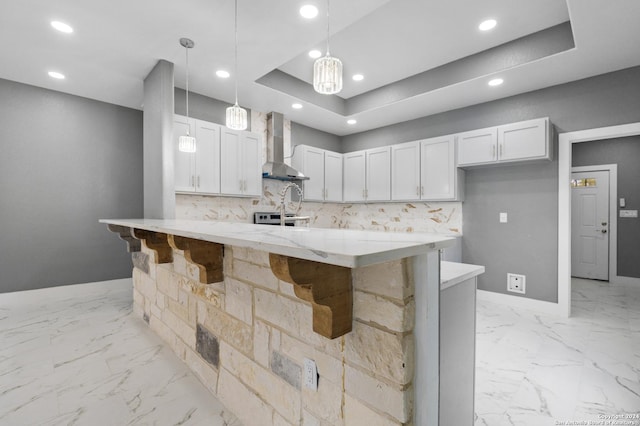 kitchen featuring backsplash, wall chimney exhaust hood, a breakfast bar, decorative light fixtures, and white cabinets