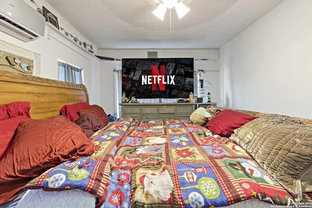 bedroom with a wall mounted AC, ceiling fan, and a textured ceiling