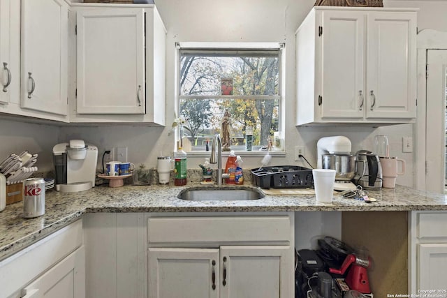 kitchen featuring white cabinets, light stone countertops, and sink