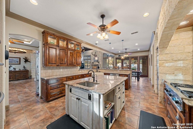 kitchen featuring pendant lighting, sink, ornamental molding, an island with sink, and light stone counters