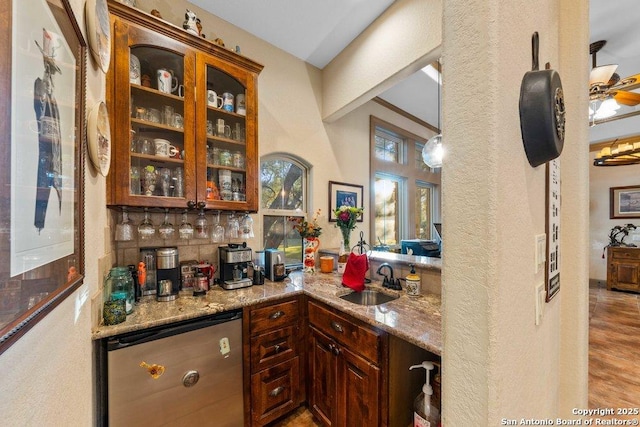 bar with light stone countertops, backsplash, sink, light hardwood / wood-style flooring, and dishwasher