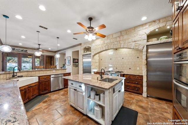 kitchen featuring sink, light stone countertops, a kitchen island with sink, and appliances with stainless steel finishes