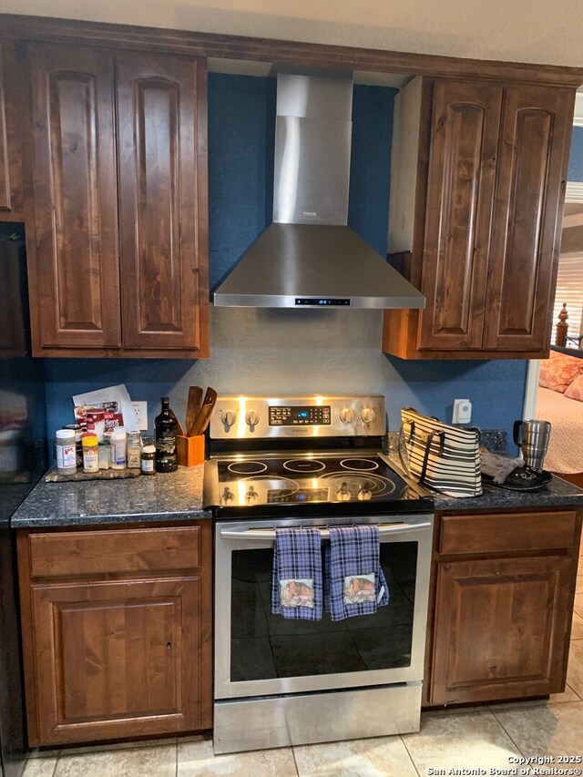 kitchen featuring stainless steel electric stove, wall chimney exhaust hood, light tile patterned flooring, and dark stone counters