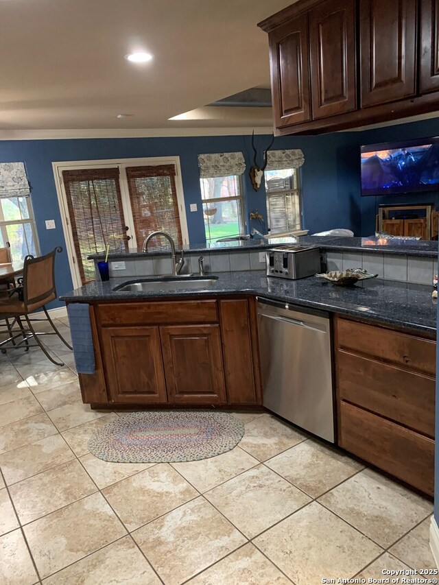 kitchen featuring stainless steel dishwasher, dark stone counters, sink, light tile patterned floors, and decorative light fixtures