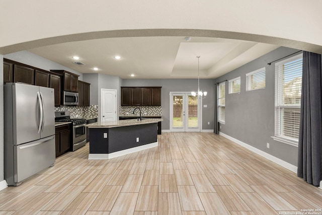 kitchen with hanging light fixtures, a raised ceiling, decorative backsplash, a center island with sink, and appliances with stainless steel finishes