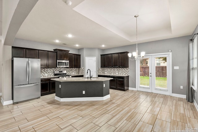 kitchen featuring a raised ceiling, hanging light fixtures, an island with sink, dark brown cabinets, and stainless steel appliances