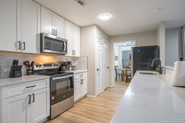 kitchen with appliances with stainless steel finishes, light stone counters, sink, light hardwood / wood-style flooring, and white cabinetry