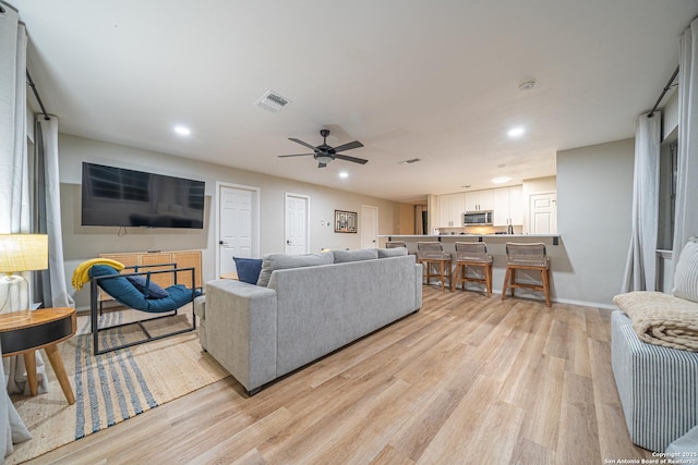 living room featuring ceiling fan, sink, and light wood-type flooring