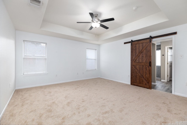 empty room with a raised ceiling, a barn door, ceiling fan, and light colored carpet