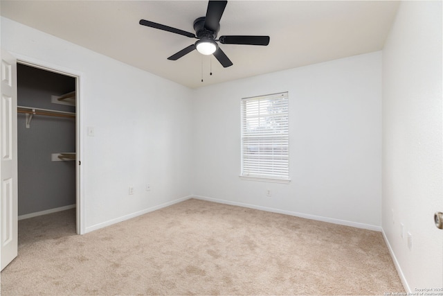 unfurnished bedroom featuring a closet, light colored carpet, a spacious closet, and ceiling fan