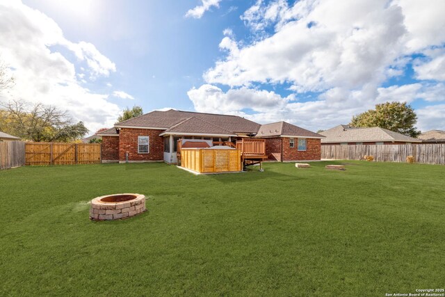 rear view of house with a fire pit, a deck, and a lawn