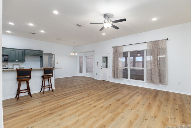 unfurnished living room featuring ceiling fan with notable chandelier and wood-type flooring