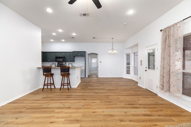 kitchen featuring a kitchen breakfast bar, light hardwood / wood-style flooring, kitchen peninsula, decorative light fixtures, and ceiling fan with notable chandelier