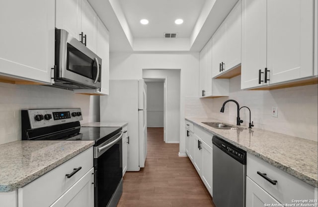 kitchen with hardwood / wood-style floors, sink, light stone countertops, appliances with stainless steel finishes, and white cabinetry