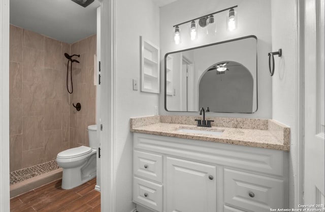 bathroom featuring ceiling fan, toilet, a tile shower, and vanity