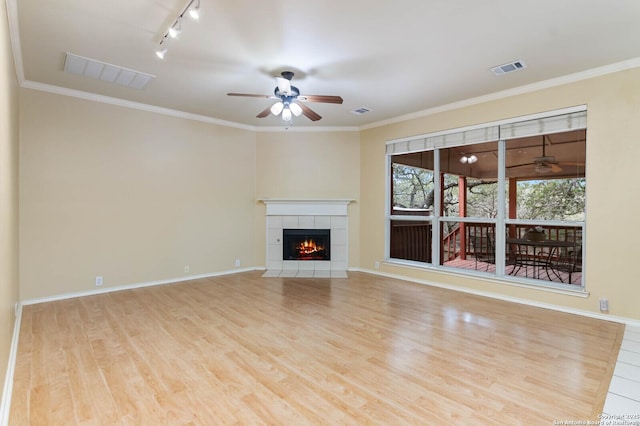 unfurnished living room with light wood-type flooring, rail lighting, ornamental molding, ceiling fan, and a fireplace