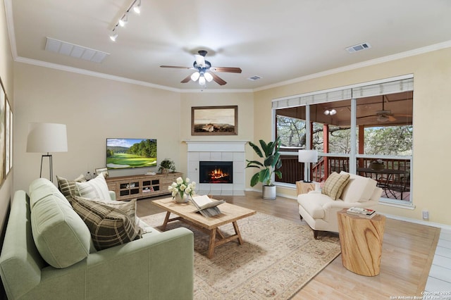 living room featuring light hardwood / wood-style floors, ornamental molding, a tile fireplace, and track lighting