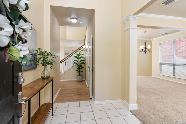 entryway featuring decorative columns, a wealth of natural light, crown molding, light tile patterned floors, and an inviting chandelier