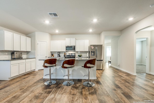 kitchen with a breakfast bar, stainless steel appliances, a center island with sink, dark stone countertops, and white cabinets