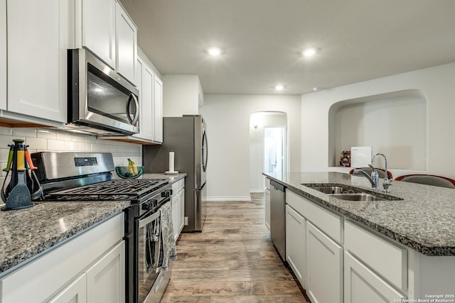 kitchen featuring light stone countertops, white cabinetry, sink, stainless steel appliances, and a center island with sink