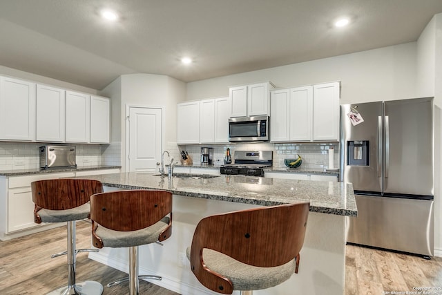 kitchen with white cabinets, a kitchen breakfast bar, sink, an island with sink, and stainless steel appliances