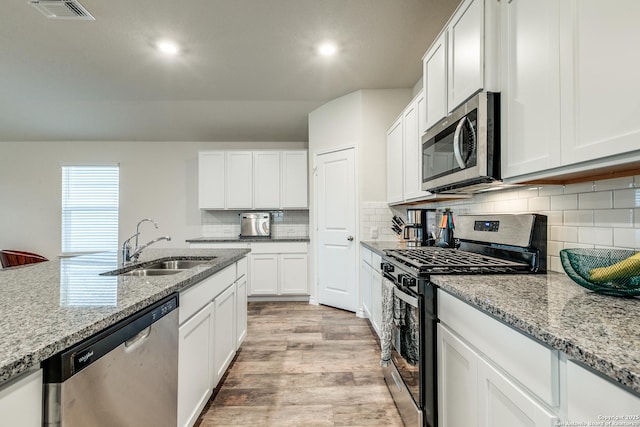 kitchen featuring light stone countertops, appliances with stainless steel finishes, sink, white cabinets, and light hardwood / wood-style floors